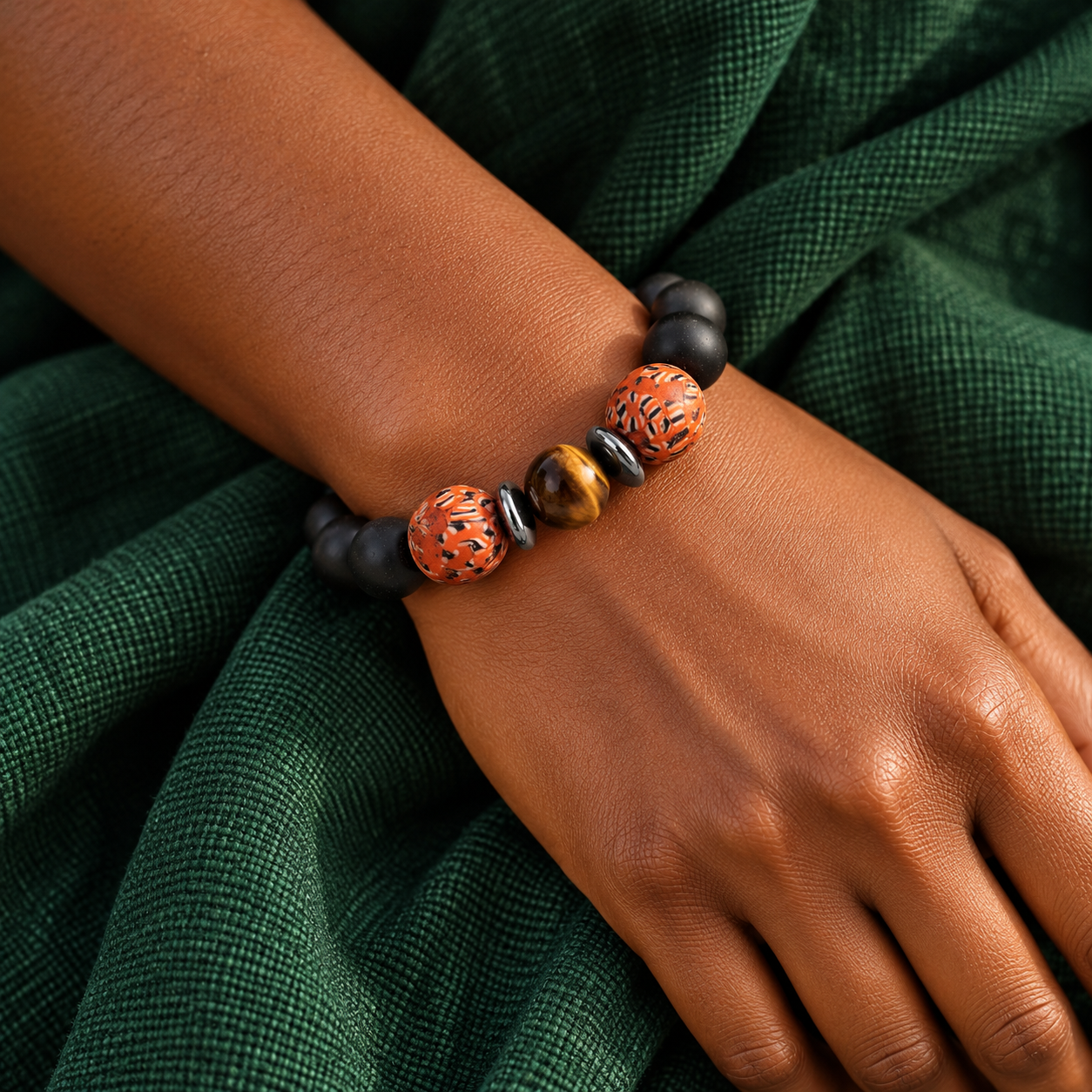 Black and gold beaded bracelet with orange patterned beads worn on a wrist
